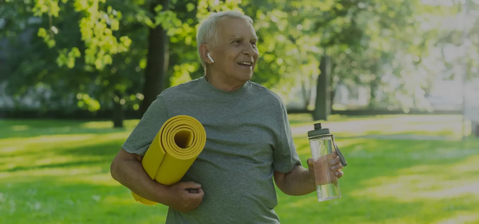 Senior man walking in a park with a yoga mat