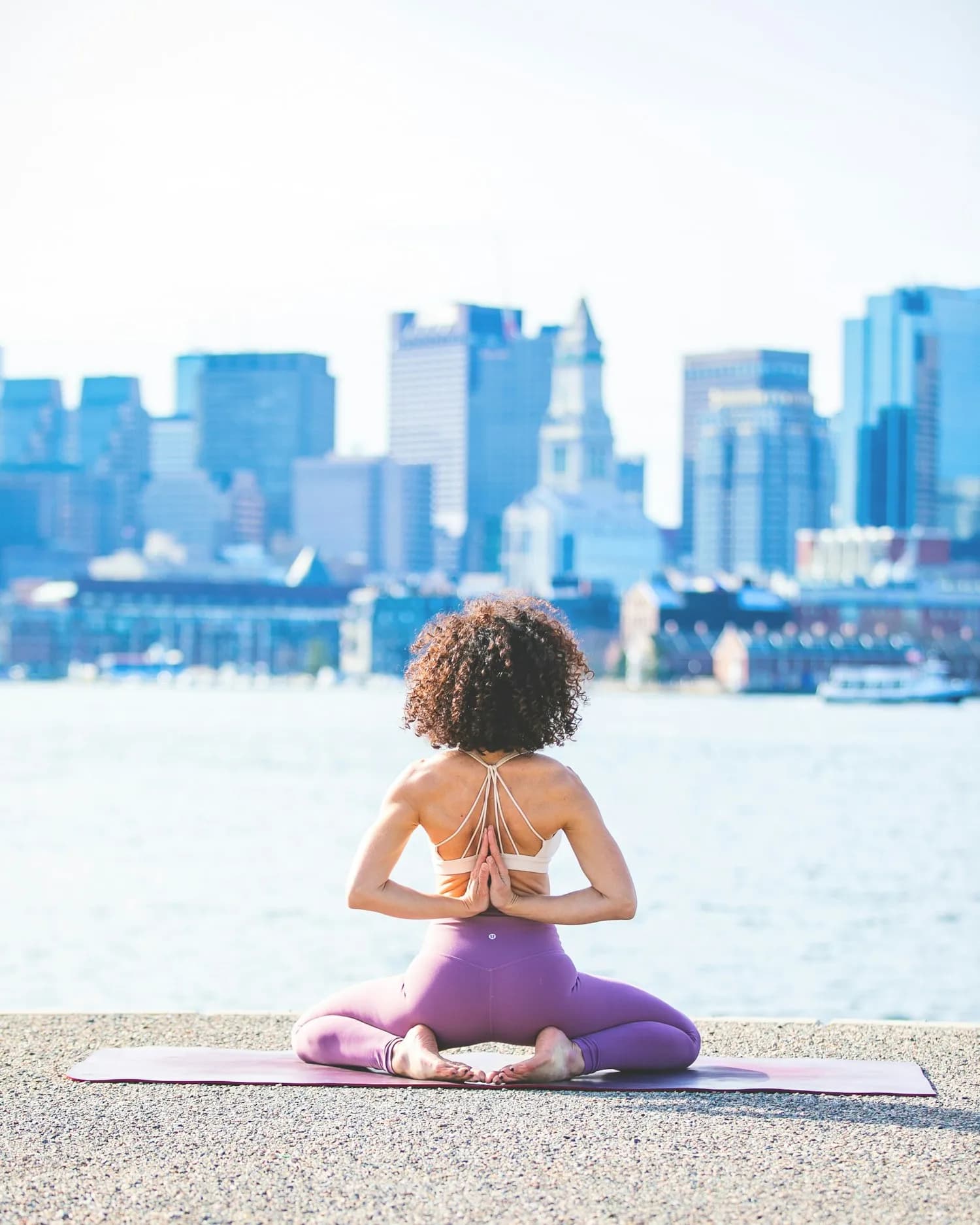 Woman practising yoga outdoors, seen from behind, facing the water