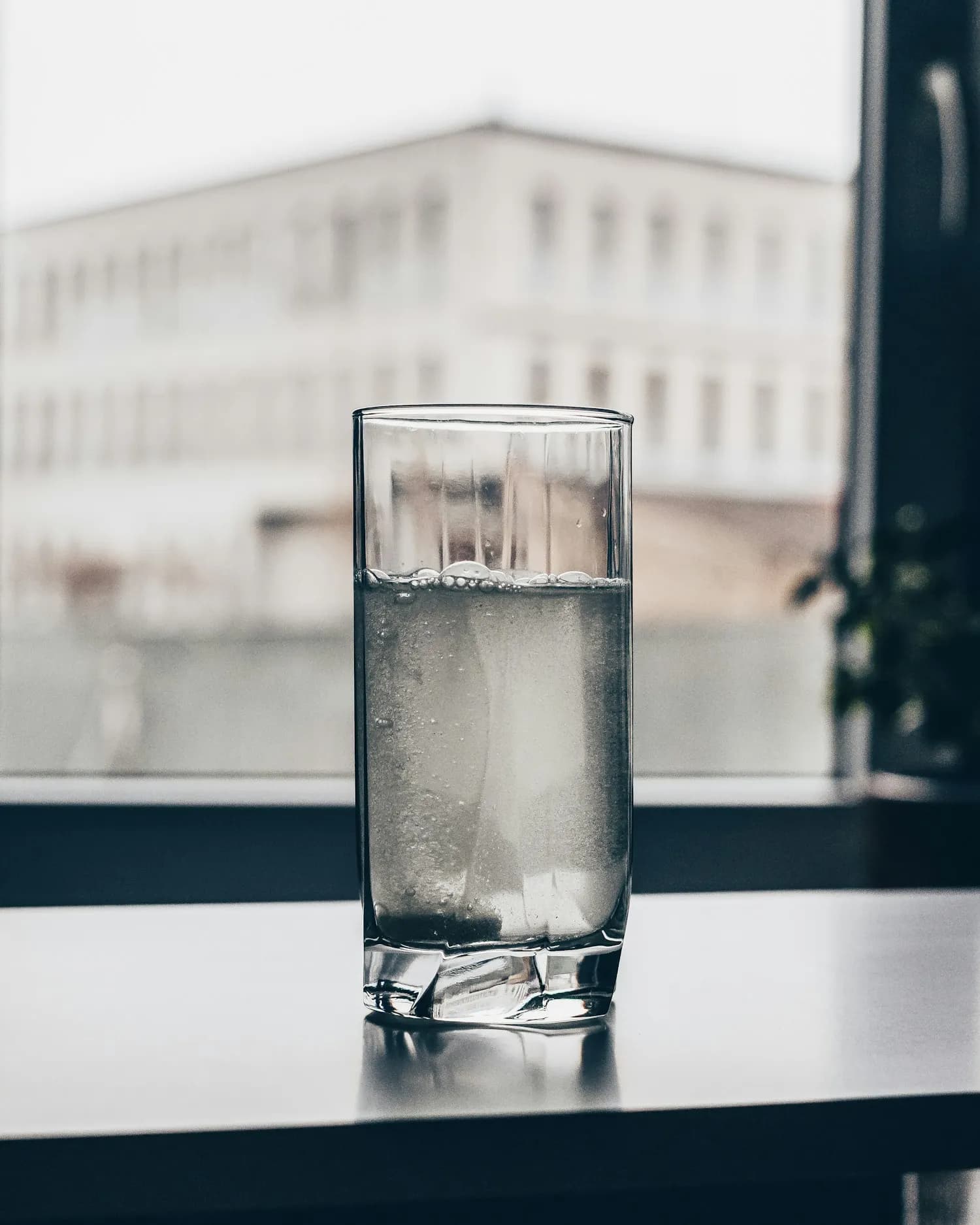 A clear glass of water on a table by a window