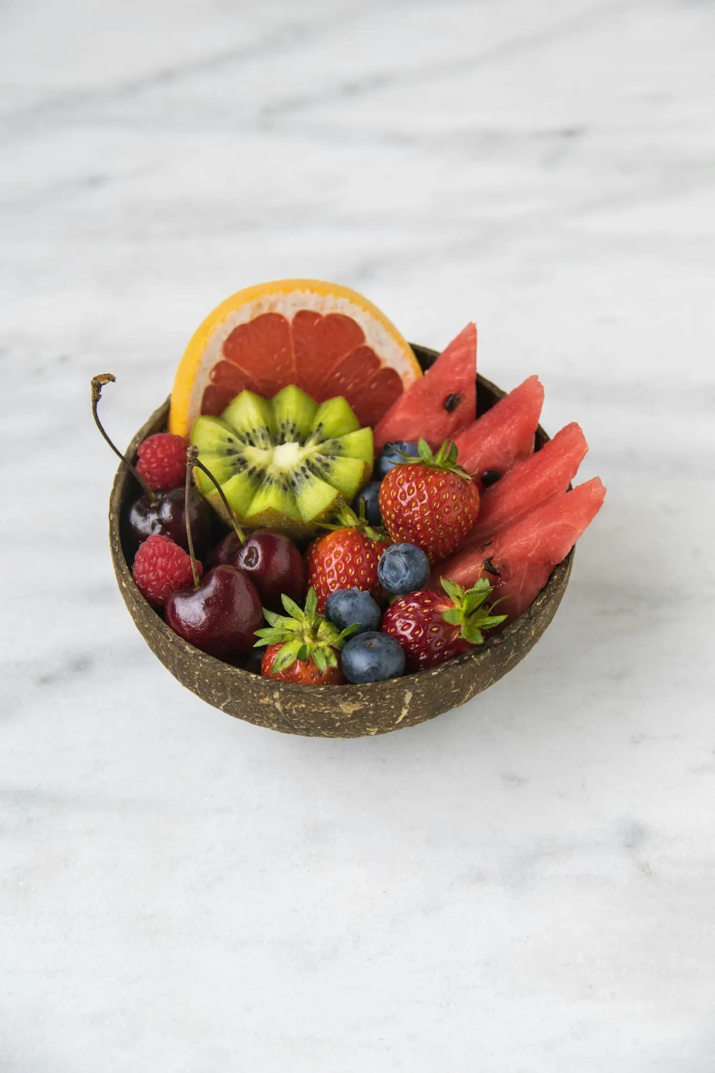 A bowl of cut seasonal fruit on a marble surface